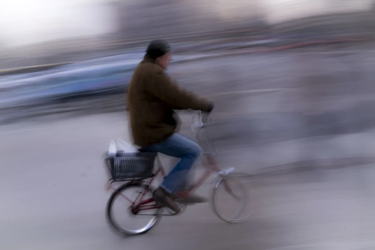 Older man riding a bicycle with a rear basket in heavy motion blur